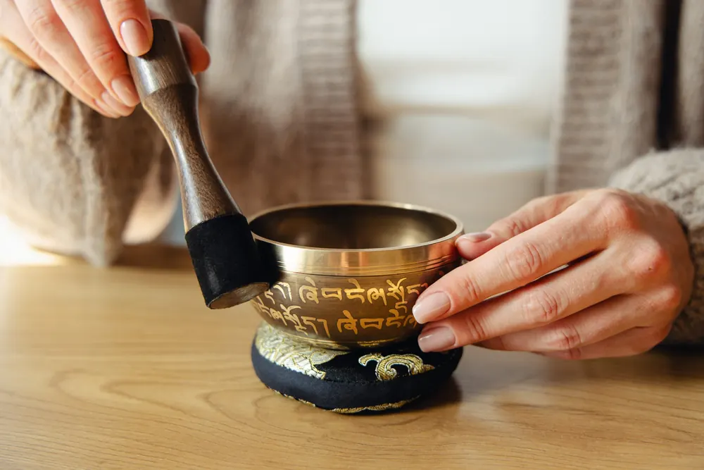 Hands playing a singing bowl resting on its cushion